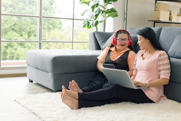 Autism and artificial intelligence: Mother and daughter seated next to each other on the floor in a living room while using a laptop and a tablet.